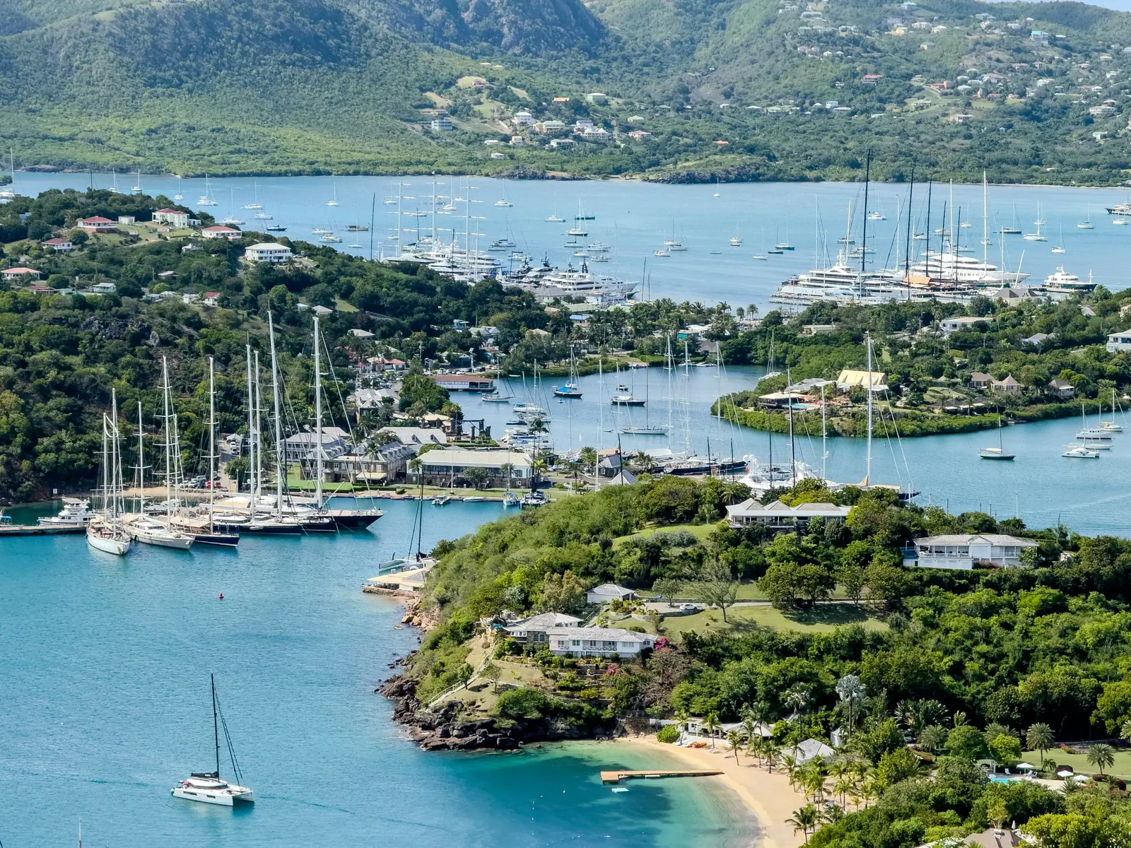 Sailing yachts moored in English Harbour, Antigua, with Falmouth Harbour and green hills behind.